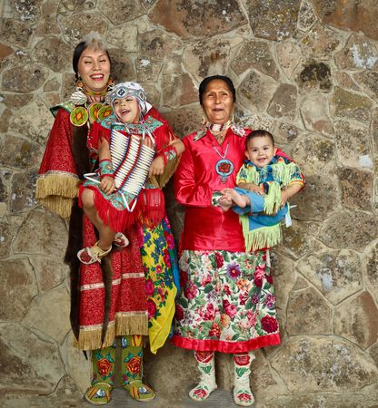 Two Native American women in traditional dress holding their children