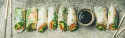 Vegetarian spring rolls lined up in a row with dipping sauce and chopsticks