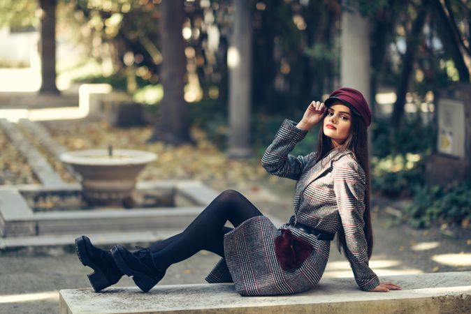 Female in warm winter clothes relaxing on park stoop looking at camera adjusting her hat