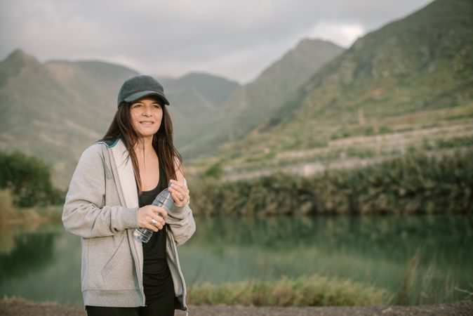 Woman drinking water near lake between mountains