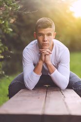 Teenager sitting leaning down on park bench looking at camera