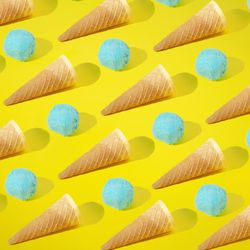 Rows of blue ice cream scoops and cones on yellow background