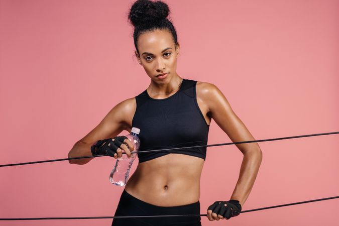 Fitness woman with rubber band and water bottle on pink background