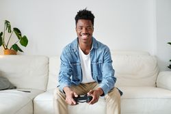 Happy Black man with joystick sitting on sofa