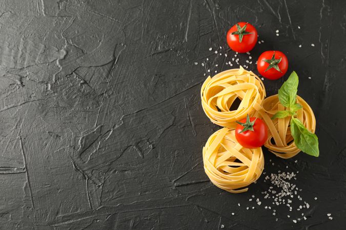 Pasta, tomatoes and salt on dark background, space for text