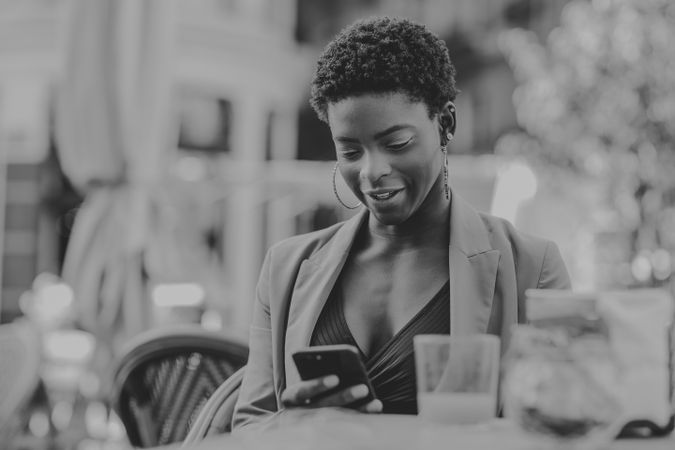 Smiling Black woman with smartphone sitting at table in cafe