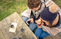 Top view of couple wrapped in blanket on cold park bench with coffee flask and muffin