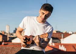 smiling man playing ukelele on a rooftop