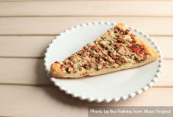 Slice of pizza with sauce drizzled on top on wooden table 5R7Gr4