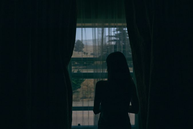 Silhouette of woman looking out window of dimly lit motel room