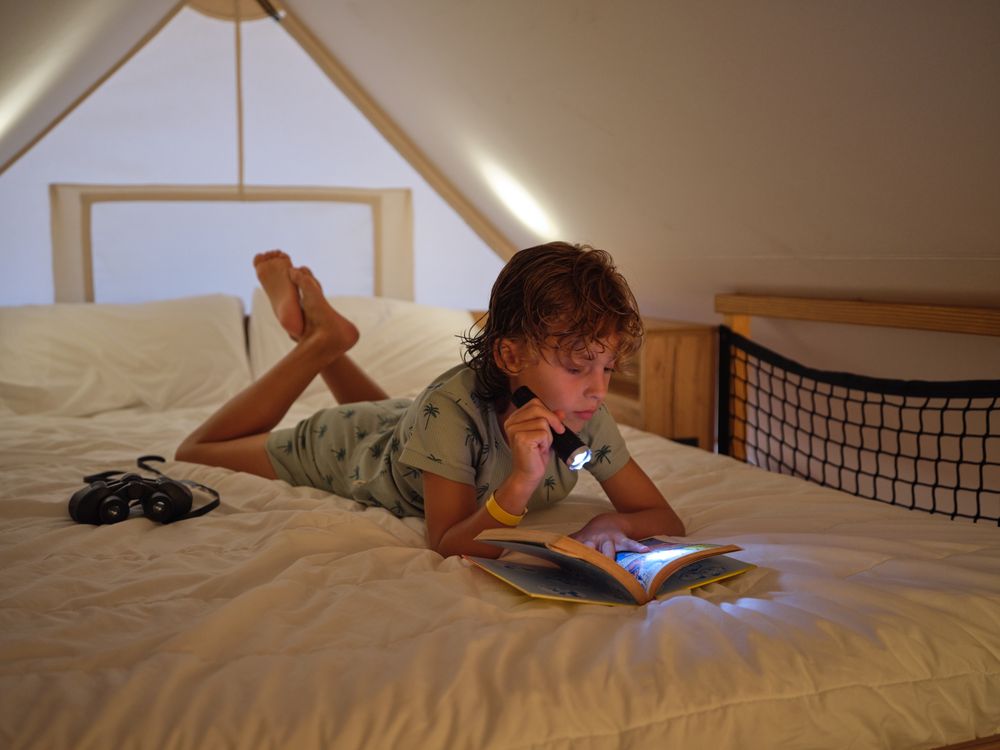 Boy reading with flashlight on bed