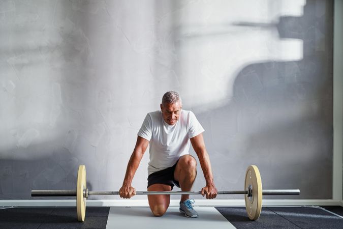 Man leaning down preparing to lift heavy barbell in bright gym