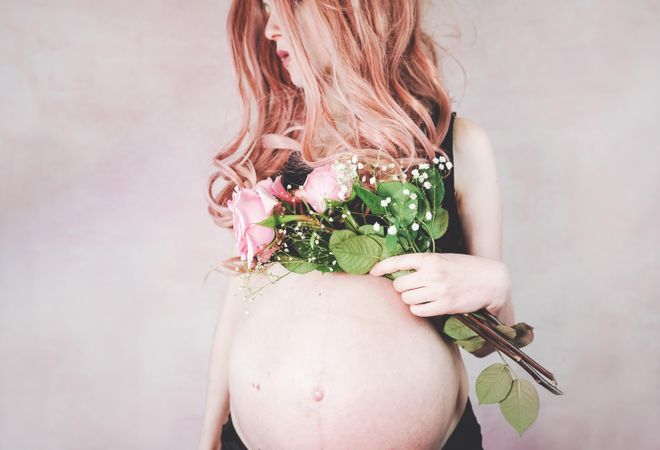 Pregnant woman with pink hair wearing crop top holding pink rose bouquet