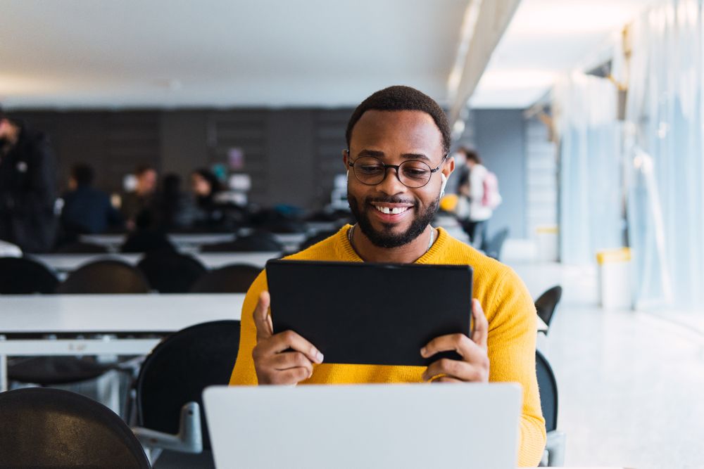 Cheerful man with earbuds using tablet and laptop at table