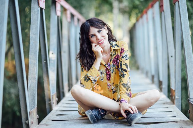 Happy female sitting cross legged on a rural bridge
