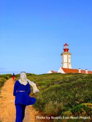 Woman in hijab walking towards lighthouse tower in Parque Natural da Arrabida in Setubal, Portugal  bGBqe4