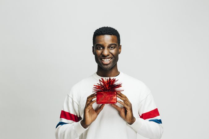 Smiling Black man holding a present wrapped in red