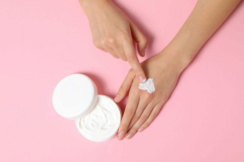 A jar of hand cream on a light pink background.