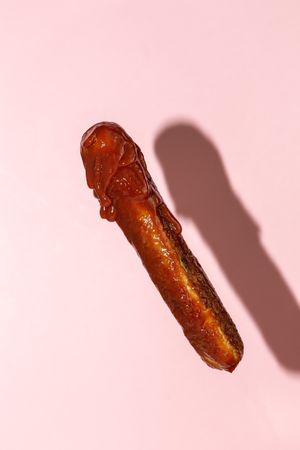 delicious grilled sausage full of ketchup in a pink background