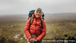 Older woman wearing jacket and backpack hiking on a hill bx71M4
