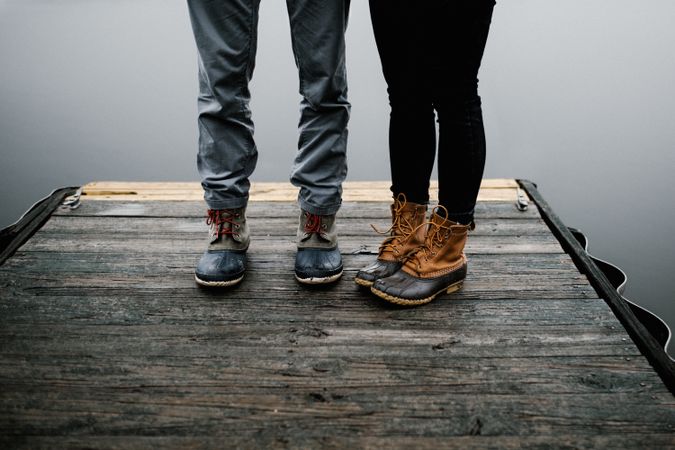 Two people standing on wooden dock beside body of water