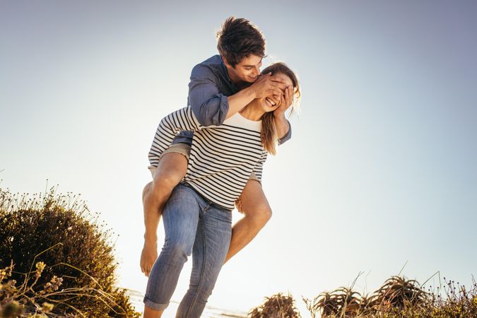 Man piggy back riding on his girlfriend closing her eyes with his hands
