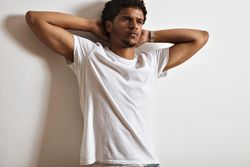 Man with thoughtful expression leaning against wall with both hands behind his head