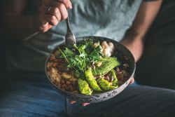 Woman in t-shirt and jeans sitting with fork in vegetarian bowl