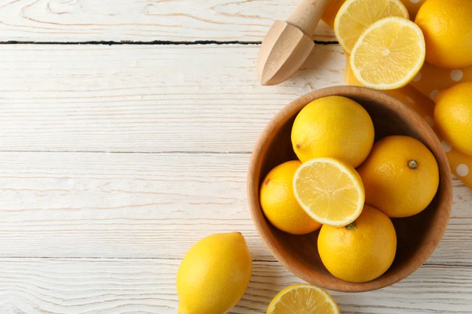 Bowl, lemons and wood juicer on wooden background, top view
