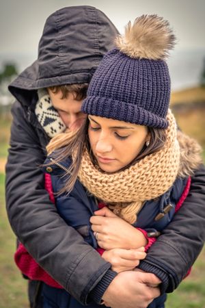 Couple dressed in warm jackets and scarfs embrace outside