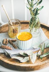 Rustic wood tray with latte cup, honey dipper in jar, kitchen towel, and vase with olive leaves
