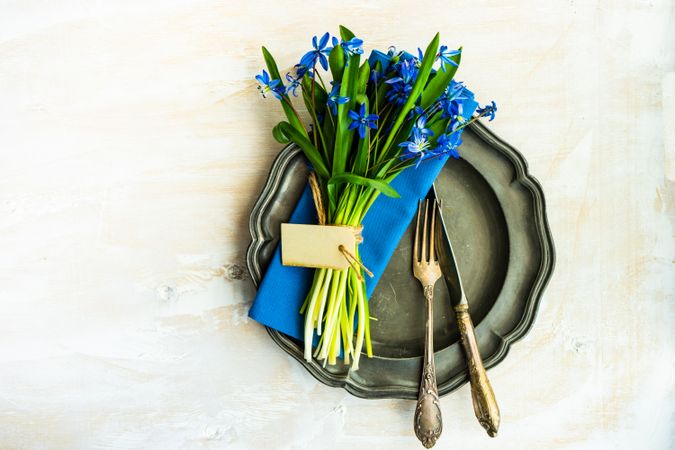 Top view of spring table setting with blue scilla siberica over blue napkin