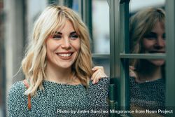 Portrait of blonde female wearing standing next to windows outside 0gnaeb