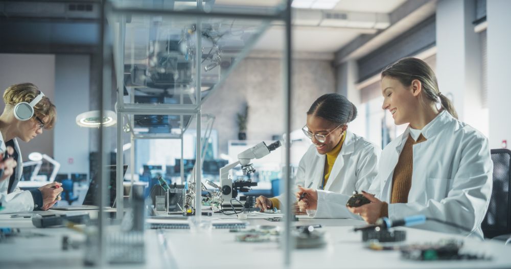 Modern Science Research Laboratory in University: Diverse Young Scientists in White Coats Using Microscopes