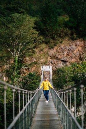 Cheerful female tourist standing on hanging bridge in summer