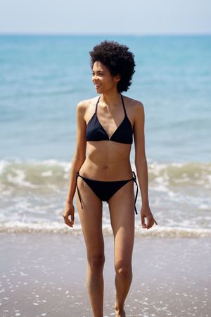 Smiling woman walking on shore in bikini looking around