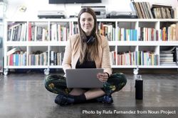 Portrait of a smiling woman sitting cross legged working on laptop with water bottle 5r9Zed