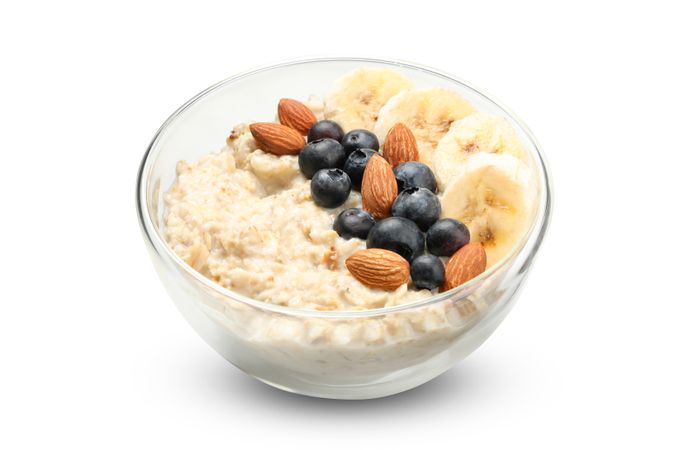 Bowl with oatmeal porridge and ingredients isolated on plain background