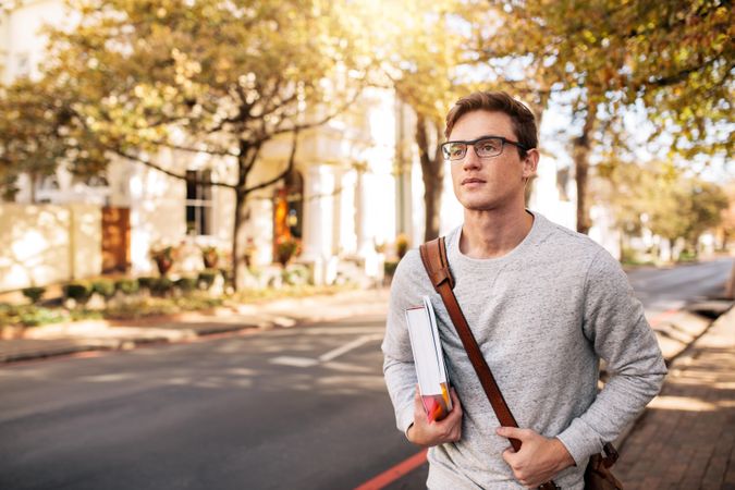 Young male student walking to class with textbook in hand