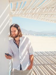 Relaxed man using smartphone in gazebo on beach