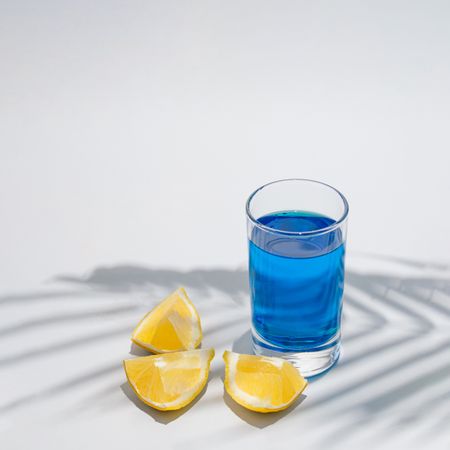 Lemon quarters with blue drink under green palm leaf shadow