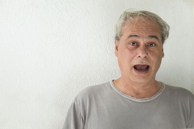 Portrait of surprised middle aged man in gray shirt against light background