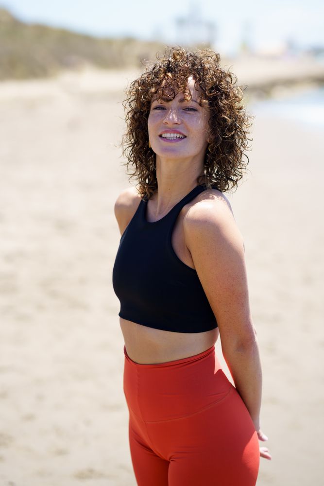 Smiling young woman in sportswear standing on beach
