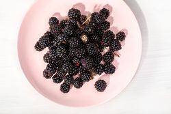 Ripe blackberry in pink plate on table