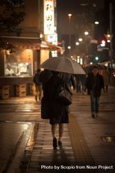Back view of person holding an umbrella walking in the street at night in Japan 0yGEa4