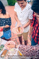 Young man holding hot dog at a barbecue with friends bE99dn