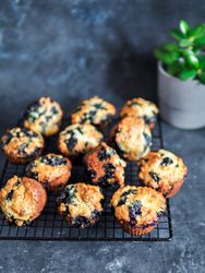 Homemade blueberry muffins on cooling rack over dark background.