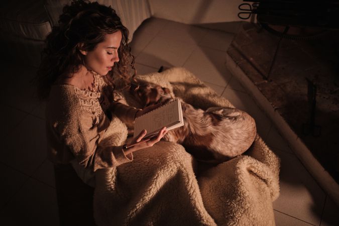 Young female reading notes in diary near fireplace with dog