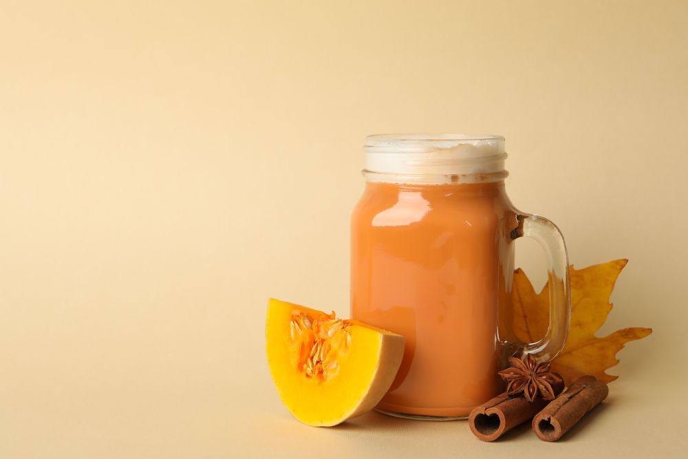 Composition with pumpkin latte, pumpkin, leaf and cinnamon on beige background