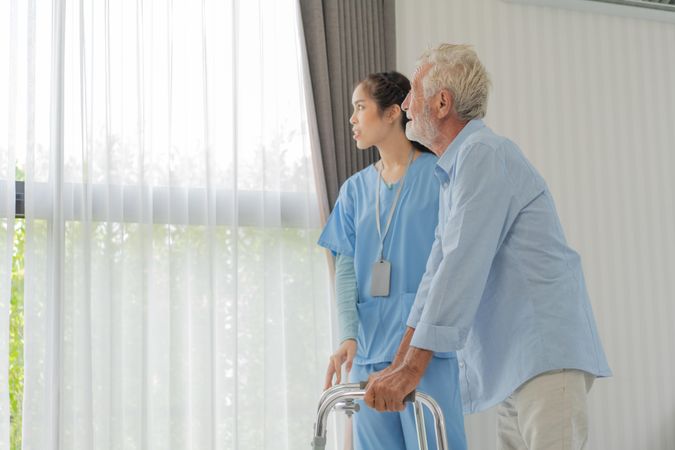 Nurse helping older male patient with walker